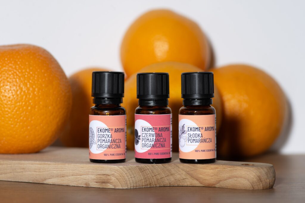 Trzy olejki pomarańczowe Ekome Aroma obok pomarańczy